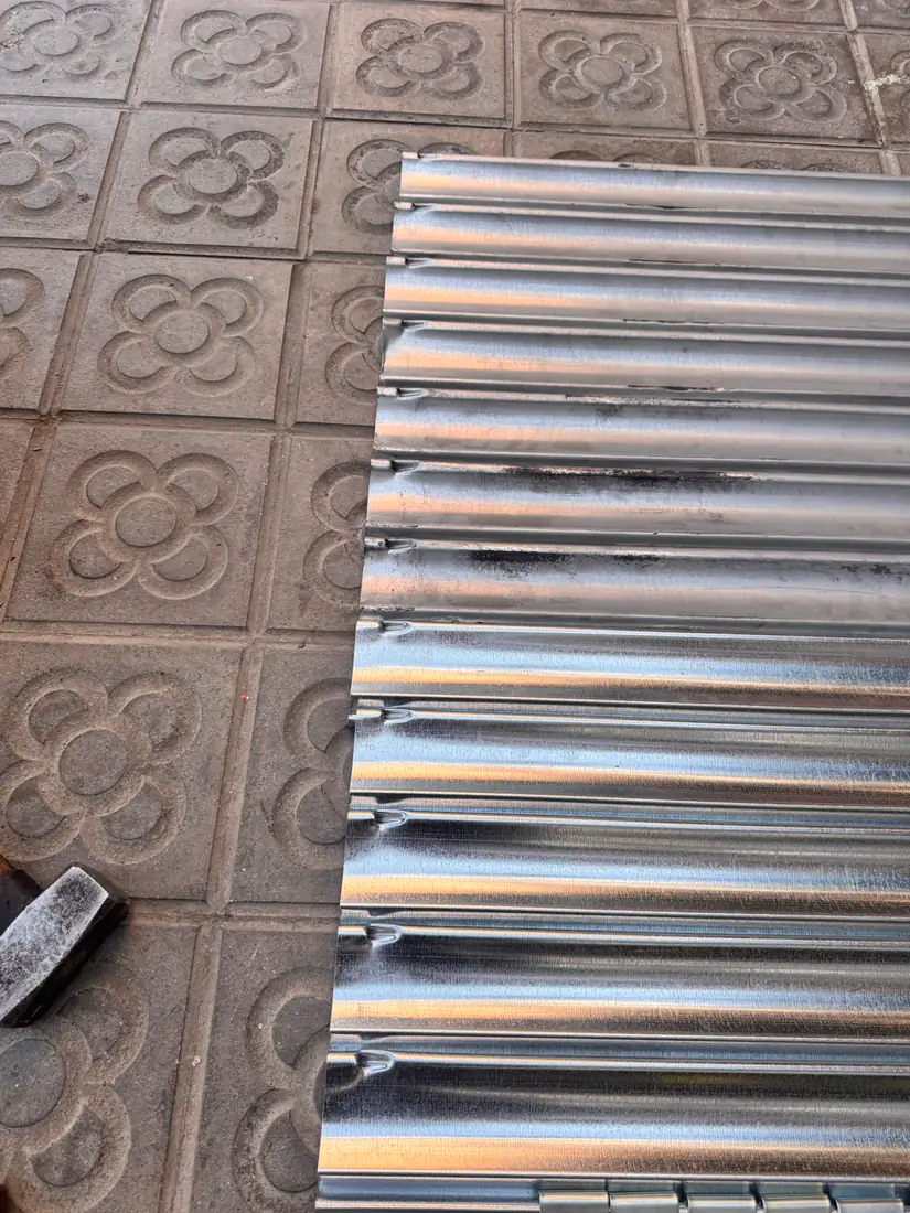 Lamel·les noves de persiana metàl·lica esteses sobre el panot d’un carrer de Barcelona abans de muntar-les